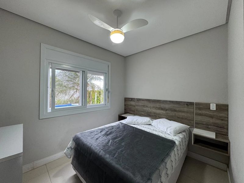 Dormitório com cama de casal, cabeceira de madeira, ventilador de teto e janela com vista para a piscina