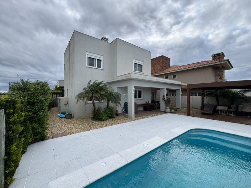 Piscina e deck com a lateral do sobrado ao fundo, em dia de céu nublado