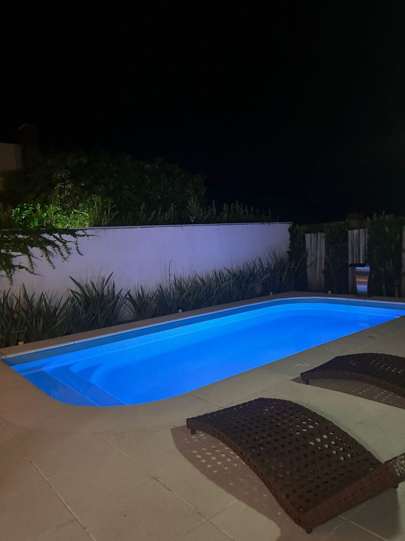 Piscina iluminada à noite, com espreguiçadeiras e muro de jardim