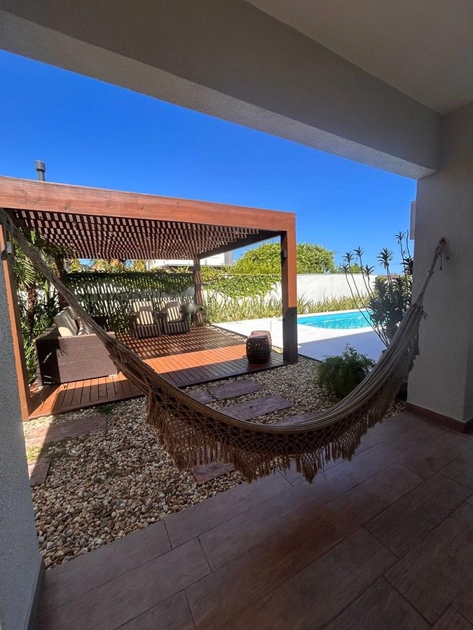 Rede de descanso sob a varanda, com o pergolado e a piscina ao fundo