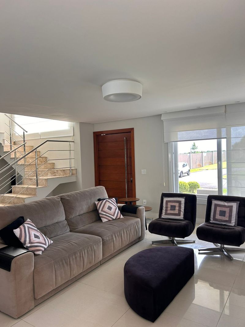 Sala de estar com sofá e poltronas, porta de entrada em madeira e escada de inox