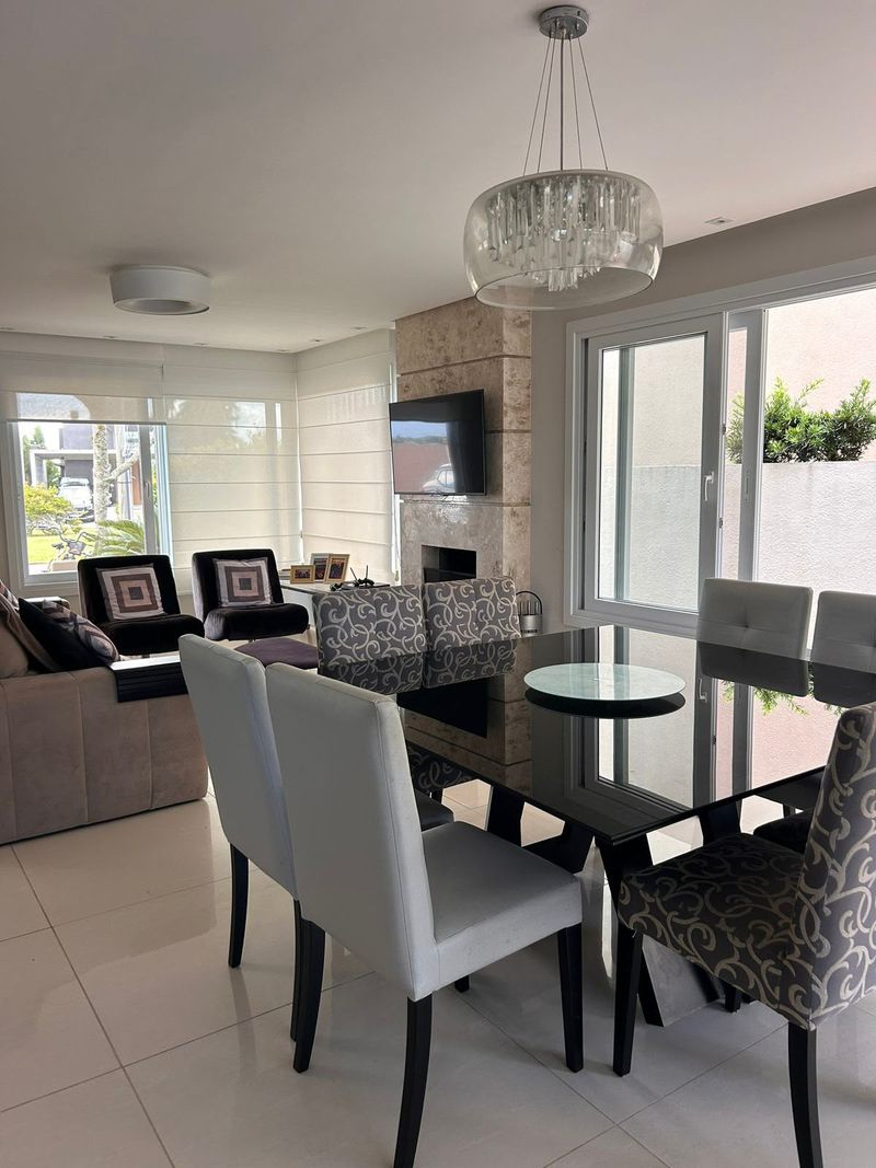 Mesa de jantar de vidro com cadeiras, lustre de cristal e sala de estar ao fundo
